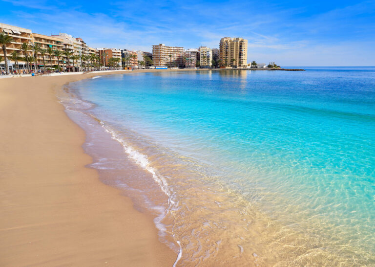 Reiseguide til Torrevieja Bildet viser stranden Playa del Cura i Torrevieja med bygninger i bakgrunnen.
